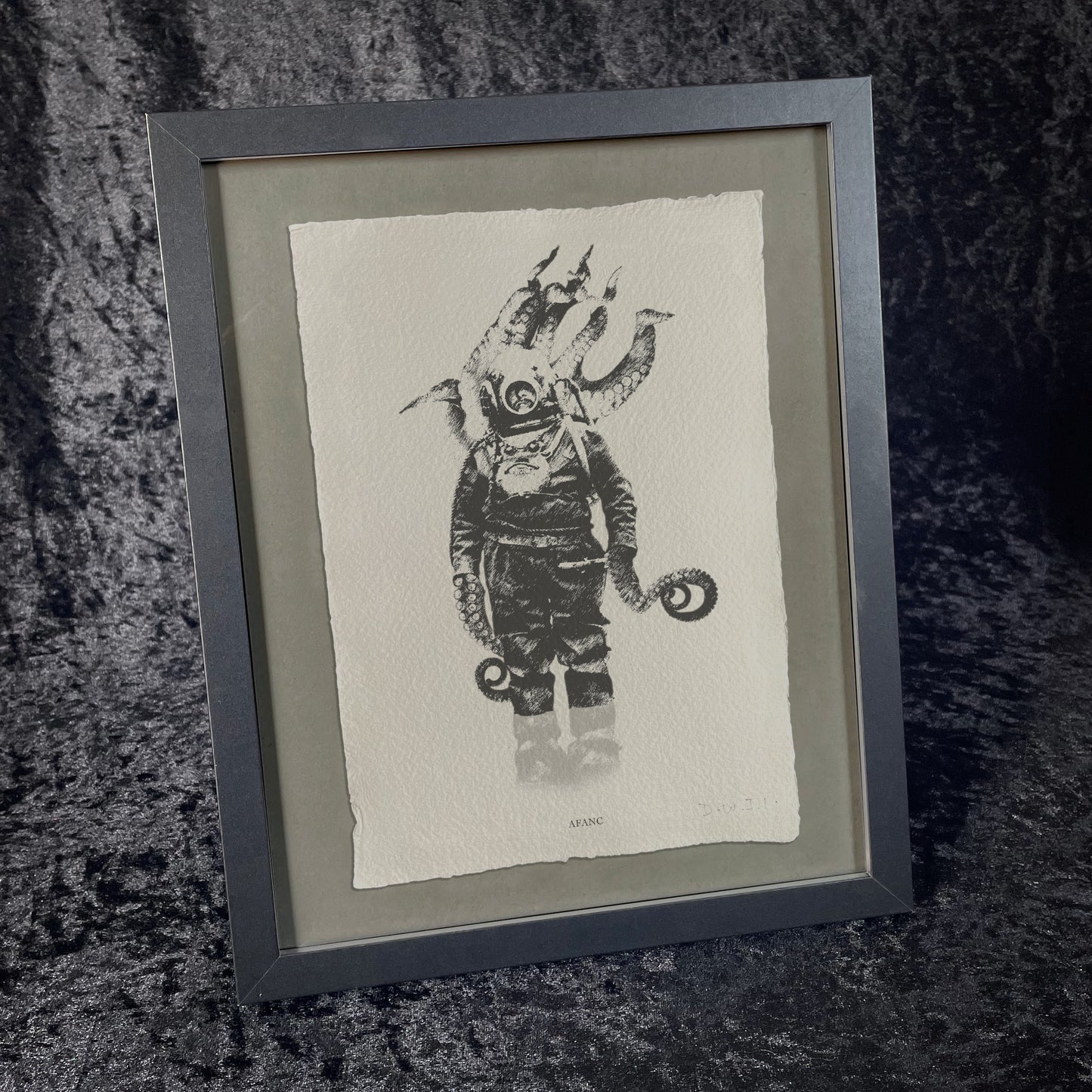 A black and white drawing of a vintage deep-sea diver in a suit and helmet, with large octopus tentacles emerging from their body. This unique wall art is printed on textured khadi paper and labelled Afanc at the bottom. This is the framed version with the print shown on a dark grey background.